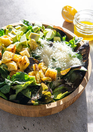 Knackiger Blattsalat mit gerösteten Ciabatta-Würfeln, Avocado und frisch geriebenem Parmesan, serviert in einer Holzschale.
