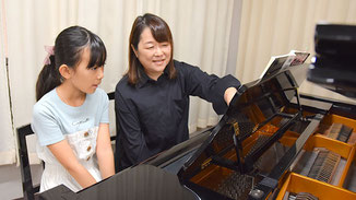ピアノ講師が子供の生徒に譜面の見方を教えている