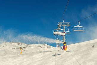 Skifahrer in den Bergen auf dem Sessellift bei blauem Himmel mit Ski- und Haftpflichtversicherung 