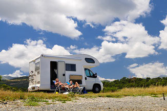 Mann und Frau lümmeln vor dem Womo im Camping-Urlaub mit Wohnmobil-Reiseversicherung der ERGO