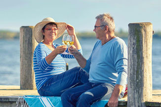 Zwei Menschen mit Weinglas in der Hand auf einem Steg am See, gut versichert mit einer Jahrespolice der ERGO Reiseversicherung