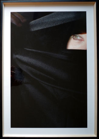 Letizia Rostagno, Il mio nome è notte #2, 2025. Frammento di autoritratto: un solo occhio verde emerge da un tessuto nero che avvolge e nasconde il volto. Una mano appare sul bordo sinistro. Stampa digitale su Canson Platine Fibre, cm 68×48, cornice in le