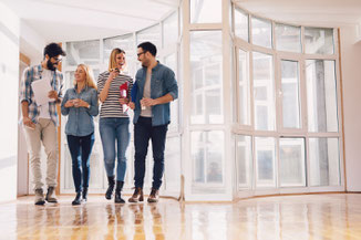Vier Menschen stehen in einem leeren Raum und warten auf den Seminarbeginn. Gut mit einer Seminarversicherung für weltweite Kurse und Seminare bei der ERGO abgesichert.