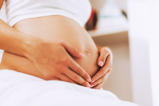 Schwangere Frau umfasst mit Händen ihren Bauch