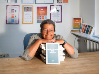 Das Bild zeigt die Übersetzerin Dr. Ruth Mader-Koltay an einem Tisch sitzend hinter einem Bücherstapel.