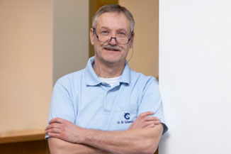 Dr. med. Michael Schwonbeck, an der Wand lehnend mit verschränkten Armen