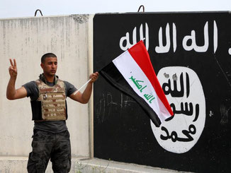 Ein irakischer Soldat in Tikrit steht mit seiner Landesflagge vor einer Wand mit dem Emblem der Terrororganisation IS. Foto: Baraa Kanaan, Archiv