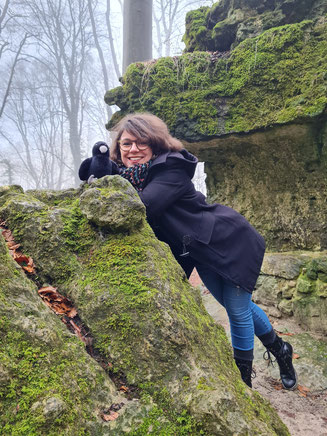 Lektorin Steffi lehnt an einem Felsen, auf dem die Krähe Krah von Rabenstein sitzt