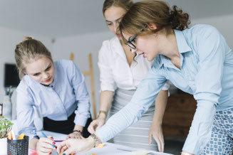 Drei Projektmitarbeiterinnen bei konzeptioneller Gestaltung am Schreibtisch.