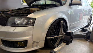 alt="graues Fahrzeug in der Werkstatt, während eine Achsvermessung durchgeführt wird."