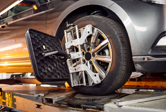 alt="graues Fahrzeug in der Werkstatt, während eine Achsvermessung durchgeführt wird."