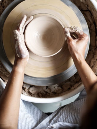 Top-down view of hands working behind the potters wheel with clay for handmade ceramics
