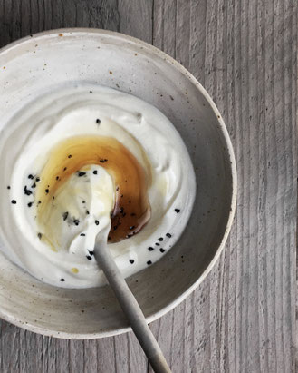 Handgemaakte keramische kom met yoghurt, een lepel en topping van honing en lavazout.