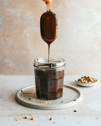 Zelfgemaakt cakebord van keramiek met een ijsje dat in vloeibare chocolade wordt gedoopt, geserveerd met een topping van gecrushte pinda’s op de achtergrond.