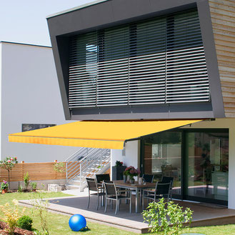 Gelbe offene Gelenkarmmarkise vor einem modernen Haus mit brauner Fassade
