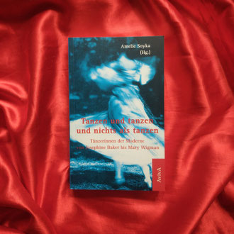Das Buch "Tanzen und tanzen und nichts als tanzen" mit einem blauen Cover, das eine Tänzerin in Bewegung zeigt, liegt auf einem roten Tuch.