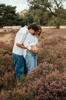 portret van zwanger koppel in de paarse heide waarbij ze allebei naar de ontblote buik kijken-zwangerschapsfotografie-©Fotografils-byIlseWagemakers-fotograaf-based in Essen, België