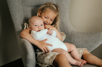 zusje zit met baby in schommelstoel en fluistert hem iets toe-babyreportage-newbornfotografie-Fotografils-by Ilse Wagemakers-fotograaf Essen