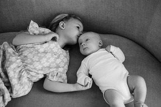 zusje ligt hand in hand met baby en geeft hem een kusje op zijn voorhoofd-babyreportage-newbornfotograaf-Fotografils-by Ilse Wagemakers-fotograaf Essen