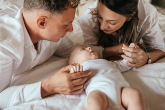 papa en mama kijken al liggend van bovenuit naar hun baby terwijl ze elk één handje vasthouden-babyreportage-newbornfotograaf-Fotografils-by Ilse Wagemakers-fotograaf Essen