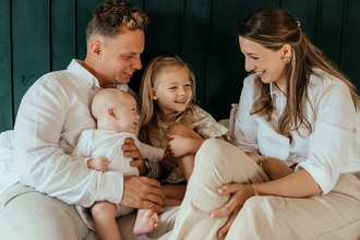 ouders met baby en zusje zitten samen op bed en lachen allemaal naar elkaar-babyreportage-newbornfotograaf-Fotografils-by Ilse Wagemakers-fotograaf Essen