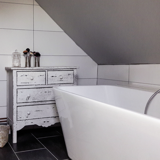 Salle de bain sous combles, dans une maison dans le Val-d'Oise, avec baignoire blanche, carrelage mural clair, meuble bois patiné et vasque moderne – rénovation et décoration intérieure.