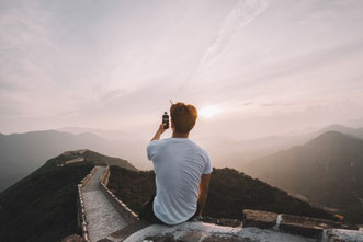 Mann sitzt mit Smartphone auf der chinesischen Mauer