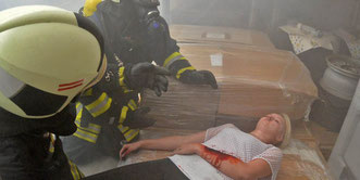 Feuerwehrmänner retten in dem verqualmten Gebäude eine verletzte Frau. Foto: Frank Gehrmann 