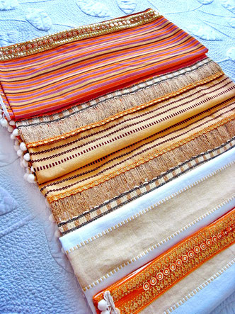 Aerial view of three-piece, orange, white and sandy striped, flat-weave, Indian cotton throw with white pom-pom trim and thick joining ribbons of orange metallic sequence and natural jute