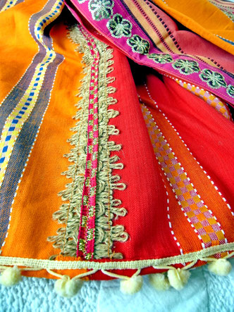 Close-up of white pom-pom trim and braided jute and pink ribbon join on three-piece, grey, red and orange striped, flat-weave, Indian cotton throw