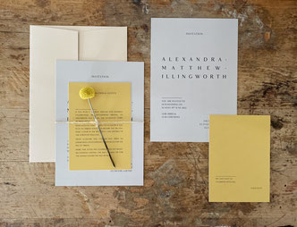 Ein Einladungskarten Set in weiß mit gelben Akzenten liegt auf einem Tisch.