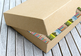 Braune Kartonschachtel mit leicht geöffnetem Deckel und Prospekten darin.