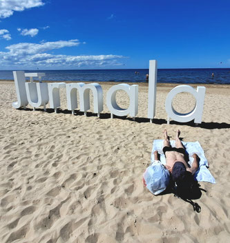 Man lying on a towel in front of big white sign saying Jūrmala on Majori Beach, Latvia