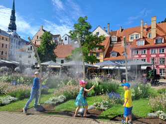 Three children playing in water sprinklers in Riga Old Town