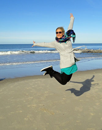 Frau, die glücklich am Strand in die Luft springt, sie hat es geschafft