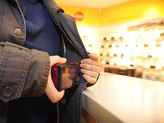 Eine Frau steckt in einem Fotogeschäft eine Kamera unter ihre Jacke. Foto: Jan-Philipp Strobel/Illustration