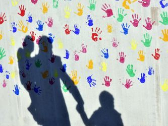 Schatten auf einer mit bunten Handabdrücken bemalte Wand einer Kindertagesstätte. Foto: Peter Kneffel/Illustration