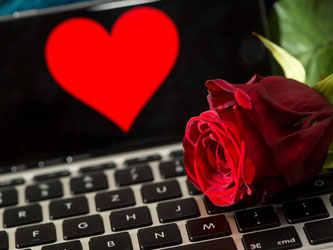 Rose liegt auf Computertastatur vor einem Smartphone mit abgebildetem Herz. Foto: Sven Hoppe/Archiv
