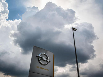 Eine einzelne dunkle Wolke schwebt in Rüsselsheim über einem Firmenlogo am Stammsitz von Opel. Foto: Frank Rumpenhorst/Illustration