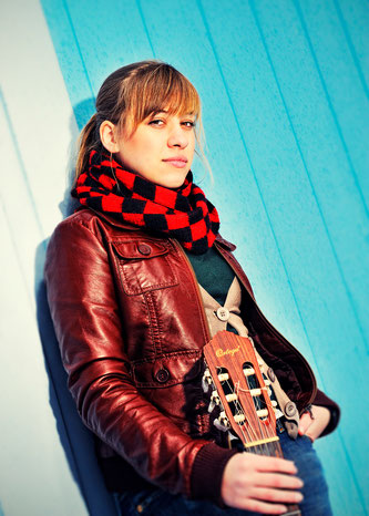 Lena Dobler lehnt mit ihrer Gitarre an einer weißblauen Wand.