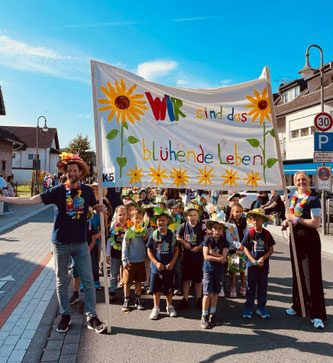 Lehrkräfte, die ein großes Banner mit Wir sind das blühende Leben hochhalten. Darunter stehen einige Kinder