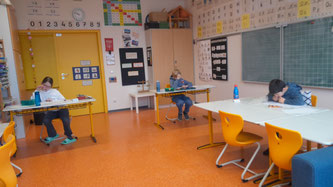 Drei Kinder sitzen an Tischen und arbeiten konzentriert an ihren Aufgaben