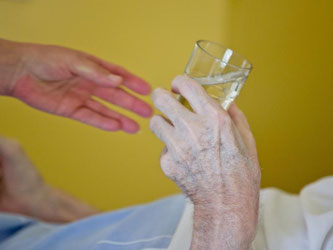 Eine Krankenpflegerin reicht einem Patienten in der Onkologie im Klinikum in Nürnberg ein Glas Wasser. Foto: Daniel Karmann/Illustration