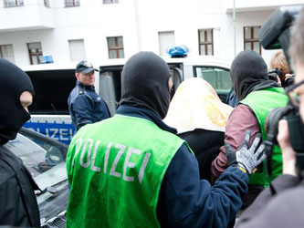 Polizisten führen in Berlin einen Verdächtigen ab. Foto: Paul Zinken