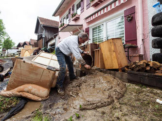 Ein Helfer kippt in Triftern einen Eimer mit Schlamm vom Hochwasser vor ein Haus. Foto: Armin Weigel