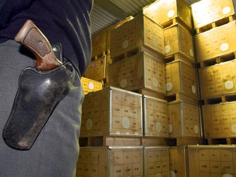 Holzkisten mit Euro-Münzen werden in einer Lagerhalle von einem bewaffneten Mitarbeiter eines Geldtransportunternehmens gesichert. Foto: Holger Hollemann/Archiv