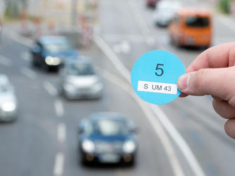 Eine Hand hält einen Designvorschlag vor vorbeifahrenden Autos. Foto: Bernd Weißbrod