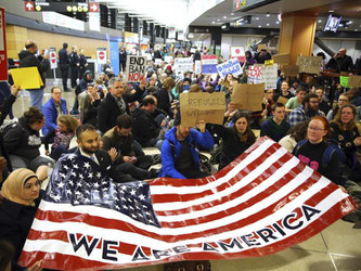 Demonstranten sitzen im Flughafen von Seattle auf dem Boden und halten ein Plakat mit der Aufschrift "Wir sind Amerika". Foto: Genna Martin