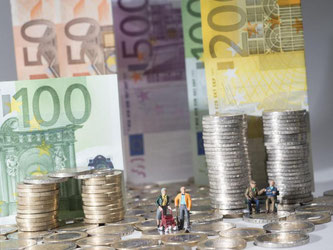 Mehrere Spielfiguren vor einer Stadt aus Geld. Foto: Oliver Berg/Archiv