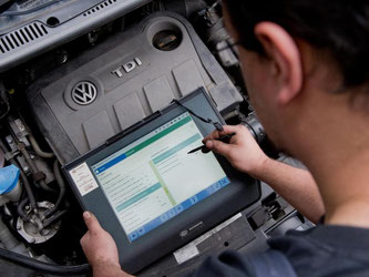 Ein Techniker steht mit einem Auslesegerät vor einem VW Touran. Foto: Julian Stratenschulte/Archiv